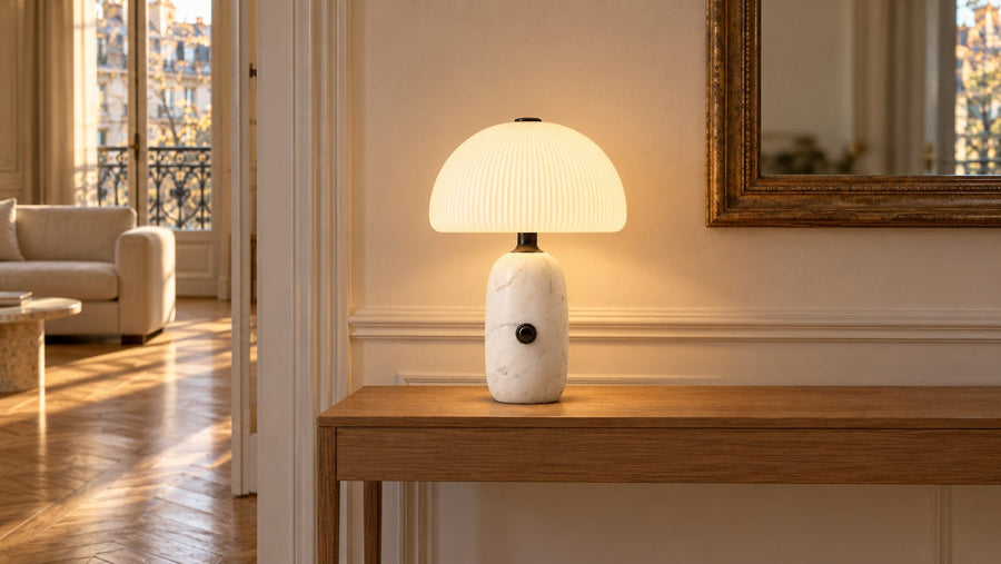 La lampe Carrara à pied en marbre blanc veiné allumée sur une console, dans un salon parisien en fin d'après-midi.