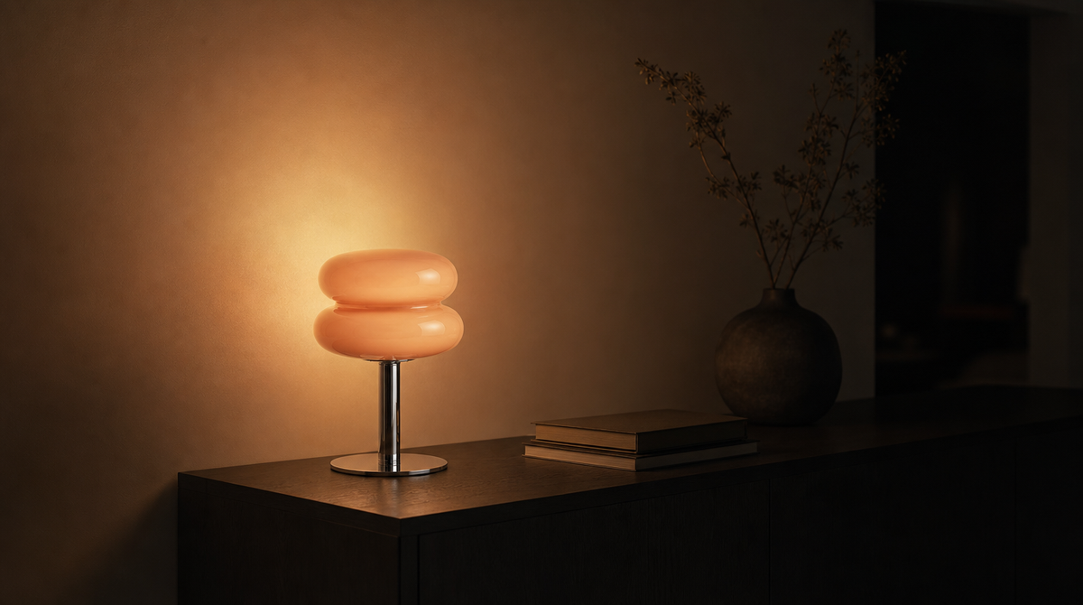 Console sombre le soir, lampe à deux dômes de verre rose allumée, sa lumière lave le mur clair derrière elle