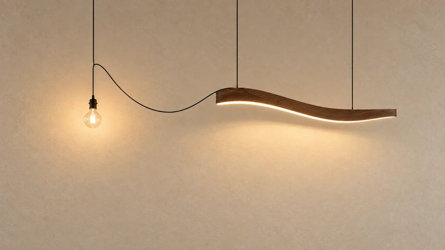 Une ampoule à filament reliée par un câble à une ligne lumineuse LED sculpturale, sur un mur clair.