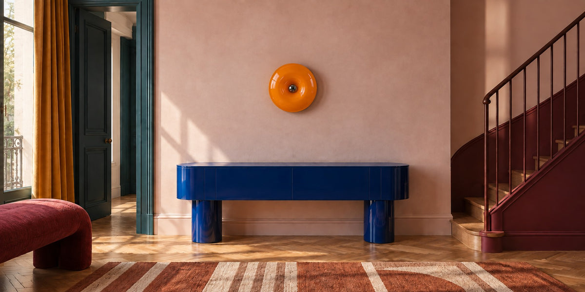 Lampe Orbita orange allumée au mur d’une entrée, au-dessus d’une console bleue